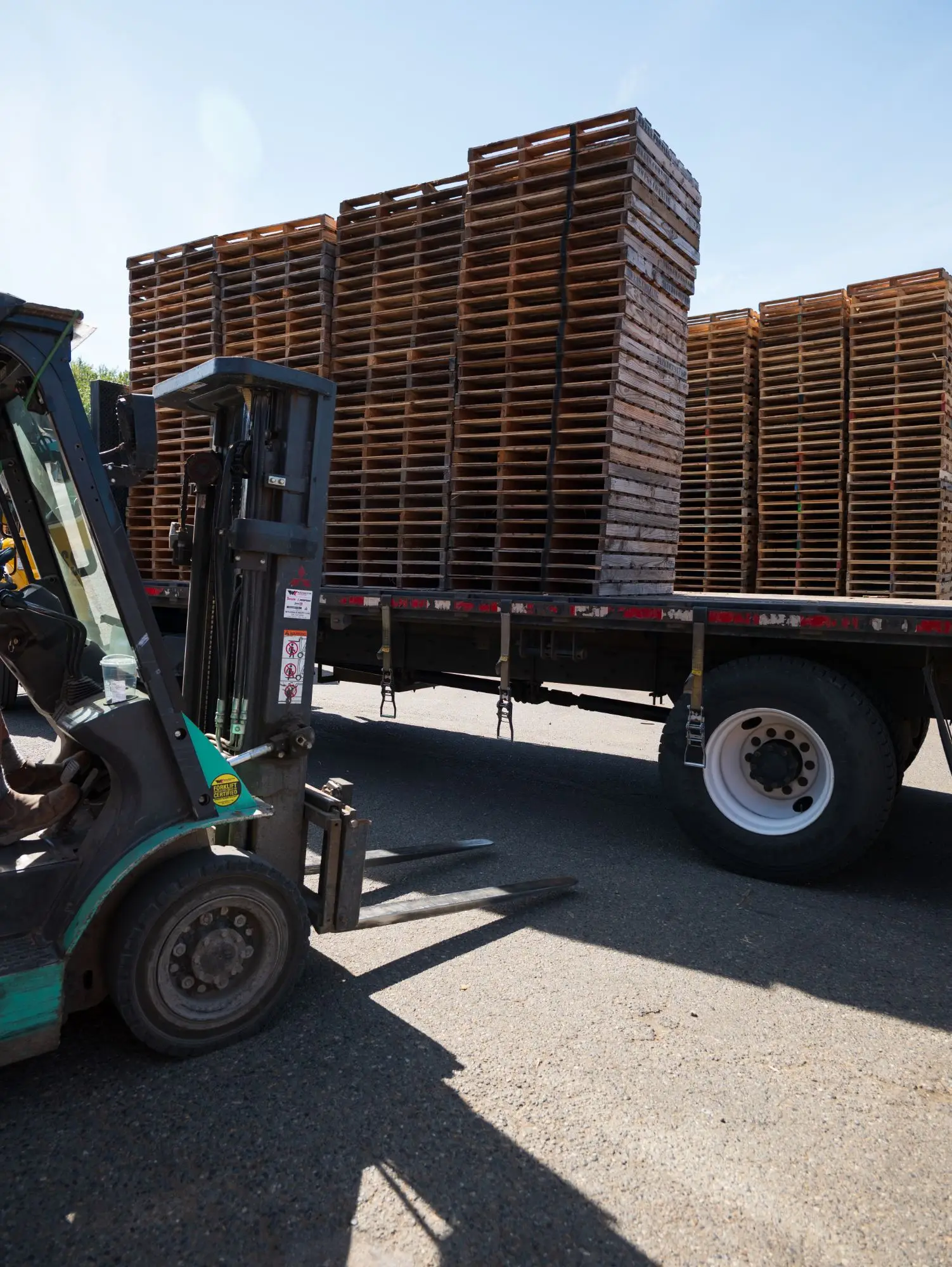 An APSS forklift loading a flatbed trailer with wood pallets at the Tacoma, WA yard